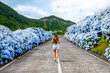 Azores, Young woman running in the middle of road with white and blue hydrangea at the roadside in Lagoa Sete Cidades (Seven Cities Lagoon), São Miguel, Açores