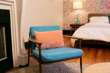 Blue cushion and wood mid century modern chair with pink pillow in bedroom, vintage pink floral wallpaper