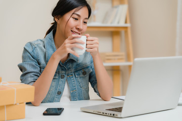 Wall Mural - Asian young entrepreneur business woman owner of SME online checking product on stock save to computer and drinking coffee working at home. Small business owner at home office concept.