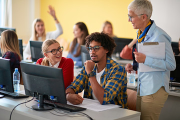 Wall Mural - Woman lecturer in computer class assisting multi-ethnic student on university.