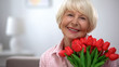 Beautiful old woman with bunch of flowers smiling at camera, birthday gift