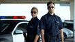 Confident policewoman and man in sunglasses standing near patrol car, on duty