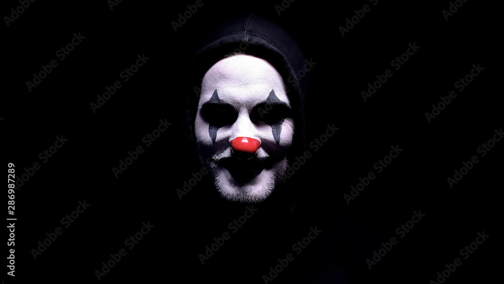 Maniac with spooky clown face angrily smiling into camera, psycho ...