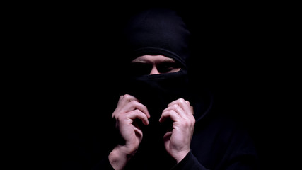 Serious man putting on balaclava, preparing for murder or robbery, banditry