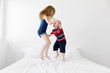 © Lisa Tichané - Brother and sister holding hands and jumping on bed