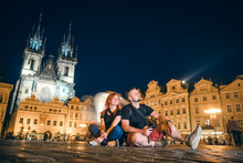 Loving Couple Sit In The Main Square, Man And Woman, Happy Together, On The Street Of The Old City Of Prague, Night Time. Historical Center. Travel And Tour In Europe, Tourism. Praha, Copy Space