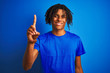 © Krakenimages.com - Afro american man with dreadlocks wearing t-shirt standing over isolated blue background showing and pointing up with finger number one while smiling confident and happy.