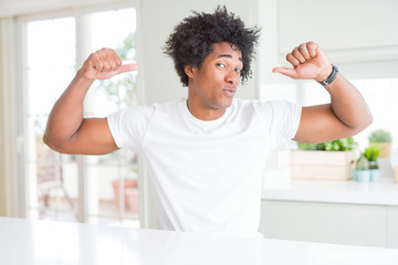 Sticker - Young african american man wearing casual white t-shirt sitting at home showing arms muscles smiling proud. Fitness concept.