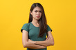 © Pormezz - Serious angry beauty asian teenager in green tee shirt folded arms isolated on yellow background in studio. Banner size and have a copy space for text.
