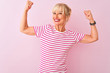 © Krakenimages.com - Middle age woman wearing striped t-shirt standing over isolated pink background showing arms muscles smiling proud. Fitness concept.