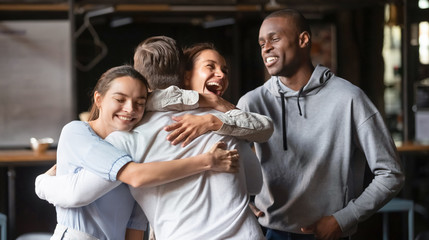 Wall Mural - Excited diverse friends embrace greeting male buddy coming at meeting