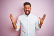 © Krakenimages.com - Young indian businessman wearing elegant shirt standing over isolated pink background celebrating mad and crazy for success with arms raised and closed eyes screaming excited. Winner concept