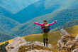 © Андрей Репетий - Young travelling girl with a backpack standing on the edge of a rock with raised hands admiring the beauty of landscape