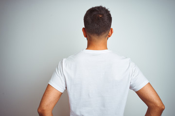 young indian man wearing t-shirt standing over isolated white background standing backwards looking 