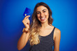 © Krakenimages.com - Young beautiful woman holding credit card over blue isolated background with a happy face standing and smiling with a confident smile showing teeth