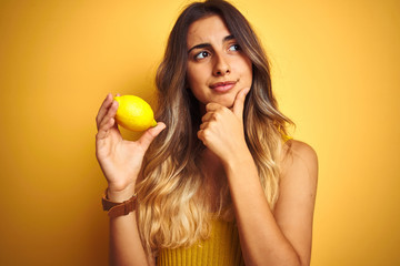 Canvas Print - Young beautiful woman eating a lemon over yellow isolated background serious face thinking about question, very confused idea