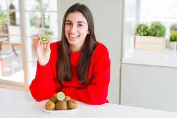 Sticker - Beautiful young woman eating half fresh green kiwi with a happy face standing and smiling with a confident smile showing teeth