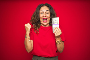 Middle age senior woman holding bunch of dollars over red isolated background screaming proud and celebrating victory and success very excited, cheering emotion