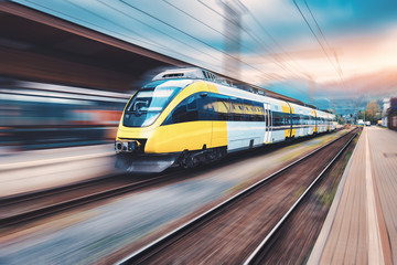 Wall Mural - high speed yellow train in motion on the railway station at sunset. modern intercity passenger train