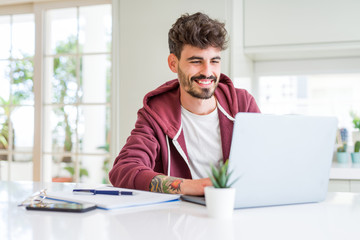 Poster - Young student man using computer laptop and notebook with a happy face standing and smiling with a confident smile showing teeth