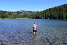 Man Wading In Todd Lake, Oregon, With Broken Top In Background On Clear Sunny Summer Afternoon.