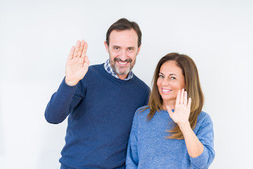 Wall Mural - Beautiful middle age couple in love over isolated background Waiving saying hello happy and smiling, friendly welcome gesture