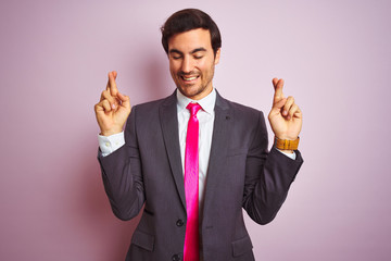 Sticker - Young handsome businessman wearing suit and tie standing over isolated pink background gesturing finger crossed smiling with hope and eyes closed. Luck and superstitious concept.