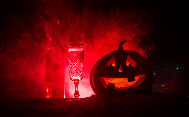 Two glasses of wine and bottle with Halloween - old jack-o-lantern on dark toned foggy background. Scary Halloween pumpkin