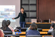 Asian Speaker or lecture with casual suit on the stage presenting via projector screen in the conference hall or seminar meeting room to Audience, business education and Seminar concept