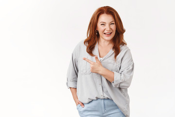 Wall Mural - Confident middle-aged redhead european woman telling about interesting product recommend check-out promo smiling toothy self-assured pointing left index finger assuring you like it, white background