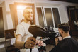 © romaset - Young man with trendy haircut at barber shop. Barber does the hairstyle and beard trim.