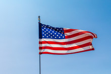 The American Flag Unfurling In Wind On Clear Blue Sky