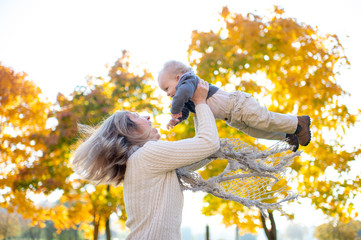 Wall Mural - Beautiful woman throws her little child up in the air in autumn park.