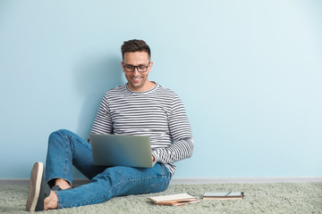 Male blogger with laptop sitting near color wall