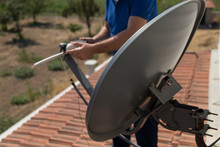 The Worker Repair The Antenna At The House Roof With Satellite Device.
