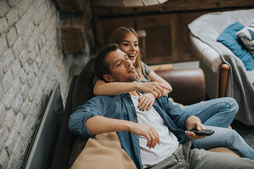 Wall Mural - Smiling young couple relaxing and watching TV at home