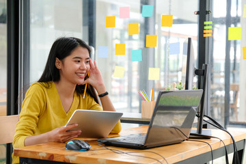 asian female programmer, wearing a yellow shirt, looking at laptop screen, holding a tablet and penc