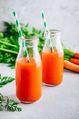 Wall Mural - Fresh detox carrot juice in glass bottles on a gray stone background