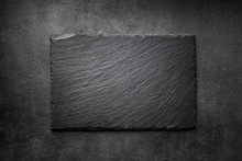 Black Slate Board On Dark Stone Texture Top View. Empty Space For Menu Or Recipe.