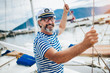 Mature man standing and laughing at helm of sailboat out at sea on a sunny afternoon.