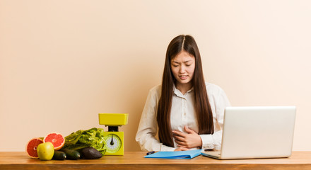 Wall Mural - Young nutritionist chinese woman working with her laptop sick, suffering from stomachache, painful disease concept.