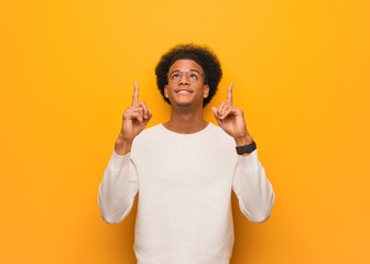 Wall Mural - Young african american man over an orange wall surprised pointing up to show something