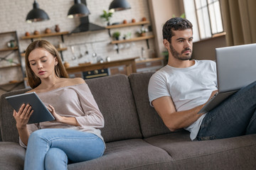 Portrait of handsome serious focused man and woman using digital tablet and laptop and don't speak with each other. Modern concept