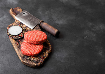 Fresh raw minced homemade farmers grill beef burgers on vintage chopping board with spices and herbs and meat hatchet on black board. Space for text