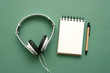 Song lyrics mockup. Music playlist. Blank page notepad and headphones on a green flat lay background.