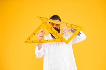 Too smart for school. Smart student of engineering faculty holding triangles on yellow background. Bearded man wearing sunglasses measuring angles with smart look. Smart math tutoring
