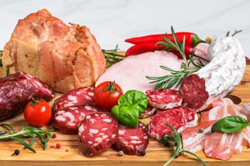 Wall Mural - Cutting board with french salami, smoked sausage, bacon, tomatoes and herbs on white marble background