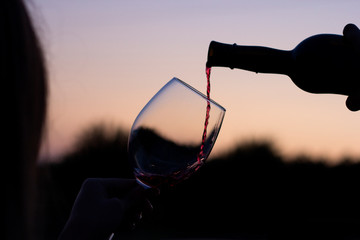 red wine is poured into a glass on a sunset background