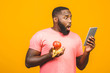 Diet concept. Healthy african american black man holding fruits isolated against yellow background. Using tablet fo searching recipe.