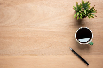 Wooden office desk table with cup of black coffee, pen and plant pot. Top view with copy space, flat lay.